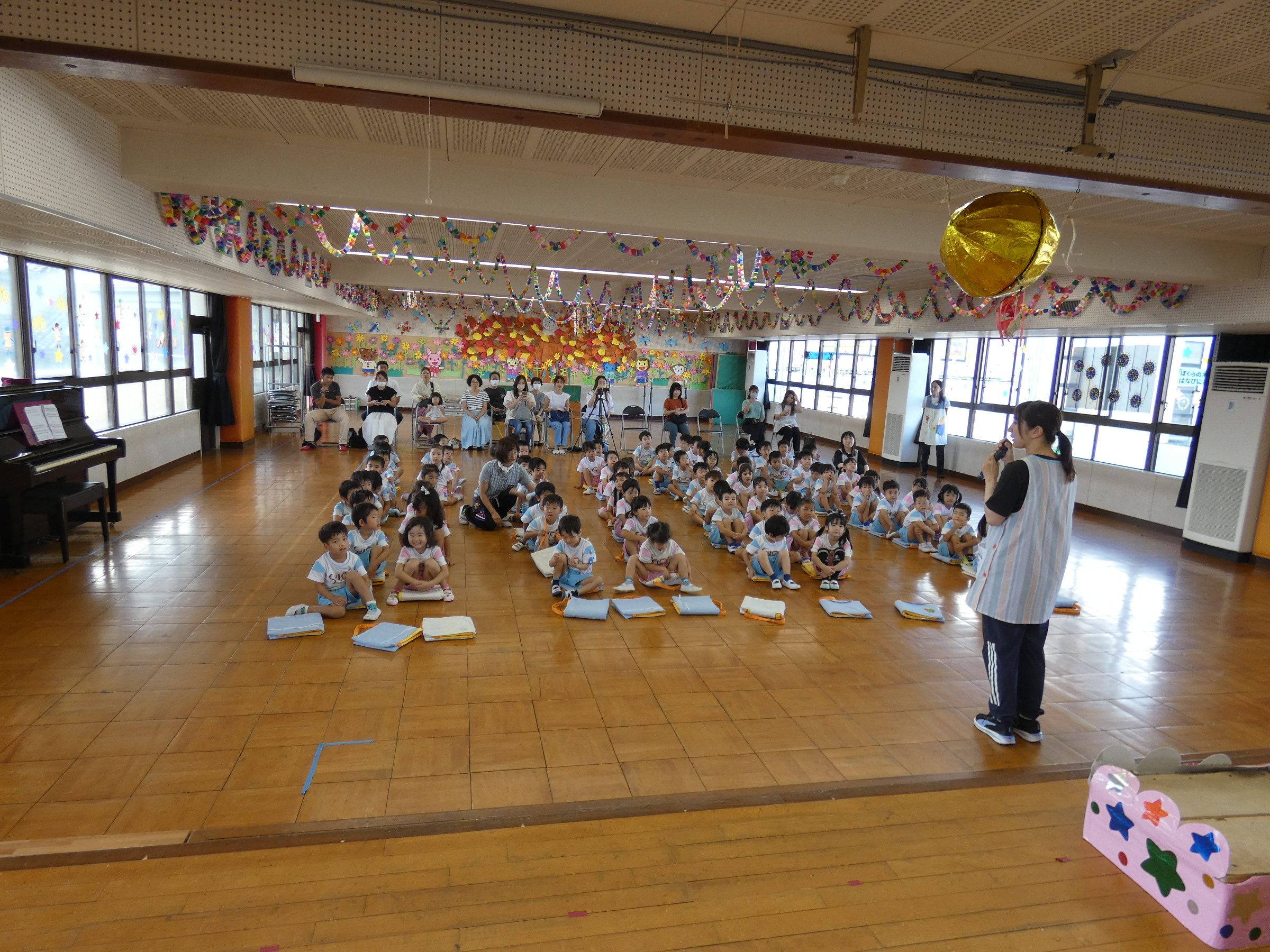 年中さんのスタートの様子です。今年から移動教室の時は万が一を考えてどの学年も防災クッション（頭巾）を持って移動してます。少し長い時間でもきちんと座ることができるようになり一石二鳥です。（特に年少さんは自分の位置が分かるのは良いことです）
